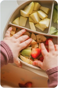 Mãos de uma criança explorando frutas durante uma refeição